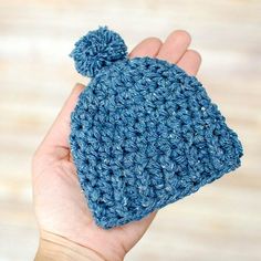 a hand holding a blue crocheted hat with a pom - pom