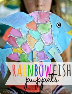 a child holding up a paper fish with the words rainbowfish puppets written on it