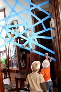 two young boys standing in front of a mirror with blue tape on the back of it