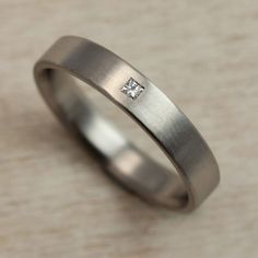 a wedding band with a princess cut diamond in the center, on a beige surface