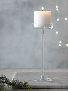 a white candle sitting on top of a table next to a christmas tree and lights