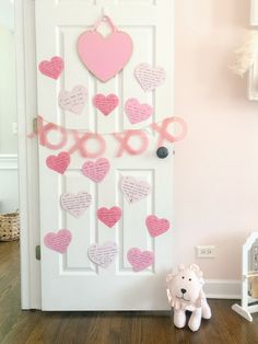 a teddy bear sitting in front of a door decorated with paper hearts and pink ribbon