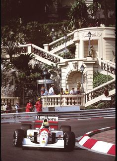 a man driving a race car down a street next to a tall building with stairs