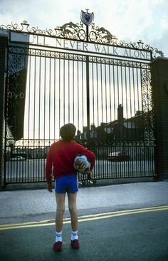 a young boy holding a soccer ball in front of a gate with an iron fence