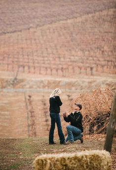 a man kneeling down next to a woman on top of a hill with trees in the background