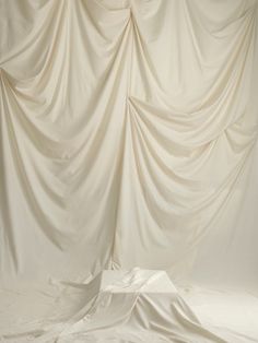 an empty photo studio with white cloth draped over the top and bottom wall, in front of a plain backdrop