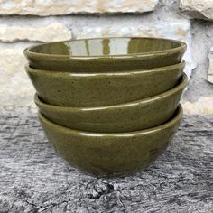 four green ceramic bowls stacked on top of each other in front of a stone wall