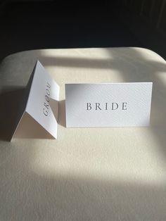 two folded white cards sitting on top of a bed next to each other with the word bride printed on them