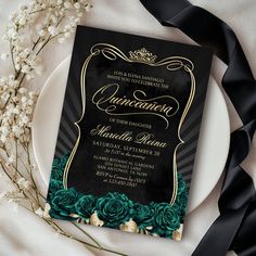 a black and gold wedding card with green roses on it next to a white plate