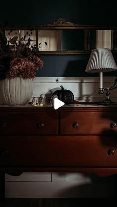 a dresser with a lamp on top of it next to a vase filled with flowers