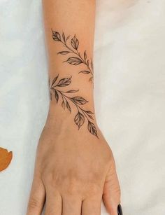 a woman's hand with a black and white tattoo on her left wrist that has leaves coming out of it