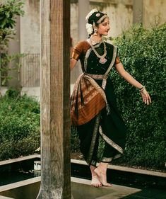 a woman standing on top of a wooden platform wearing a black and brown dress with gold accents