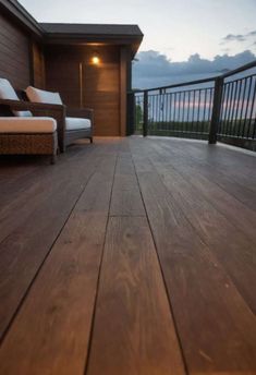 a wooden deck with two chairs and a couch on top of it at night time