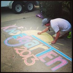 a man is drawing on the sidewalk with chalk and crayon markers in front of him