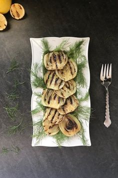 a white plate topped with grilled chicken next to lemons and a fork on top of a table