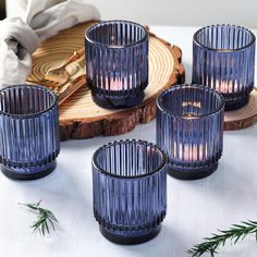 four blue glass candle holders sitting on top of a table next to slices of wood