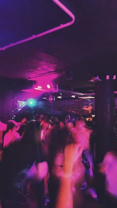 a group of people are dancing in a room with purple and blue lights on the ceiling