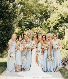 a group of women standing next to each other in front of trees and bushes with bouquets