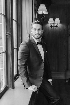 a black and white photo of a man in a tuxedo leaning on a window sill