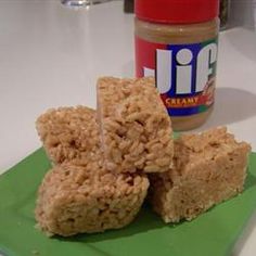 two pieces of rice krispy treats on a green plate next to a jar of peanut butter