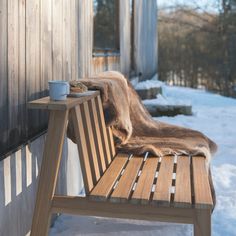 a wooden bench with a blanket on it next to a building in the winter time