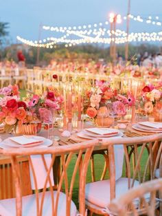 a table set up with flowers and candles for an outdoor wedding reception in the evening