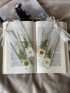 two bookmarks with flowers on them are placed next to an open book that is laying on a bed