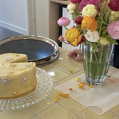 a cake on a table next to a vase with flowers in it and an empty plate