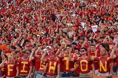 a large group of people standing next to each other in front of a stadium filled with fans