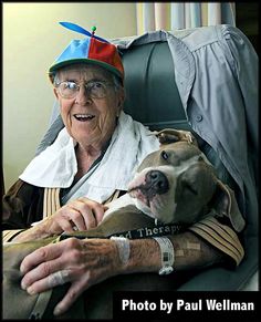 an old man sitting in a chair with a dog wearing a hat on his head