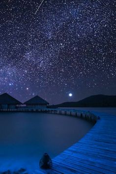 the night sky is filled with stars and bright blue water as well as some huts