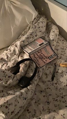 an unmade bed with a book and headphones laying on top of the sheets