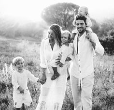 a black and white photo of a family walking through a field with one child on his shoulders