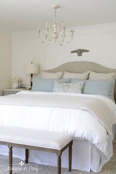 a bedroom with a white bed, chandelier and two tables in front of it