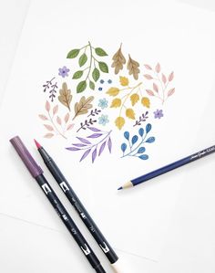 two pencils are sitting on top of a paper with watercolor flowers and leaves