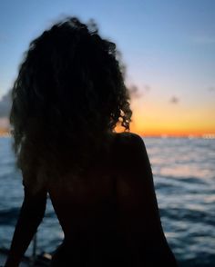 the back of a woman's head as she sits on a boat at sunset