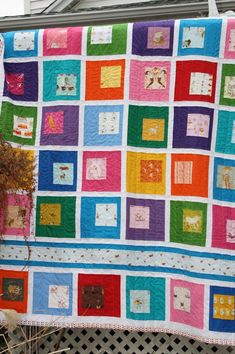 a multicolored quilt hanging on the side of a fence in front of a house