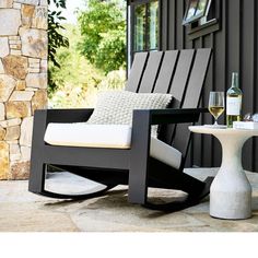 a black rocking chair sitting on top of a patio next to a table with a glass of wine