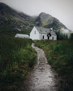 a white house sitting on the side of a lush green field next to a mountain