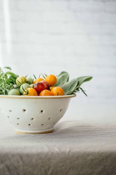 a white bowl filled with lots of different fruits and vegetables on top of a table