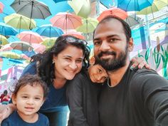 a man and woman taking a selfie with their child in front of umbrellas