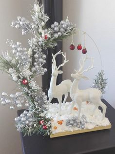 a christmas scene with white deer and red baubs on a black table in front of a mirror