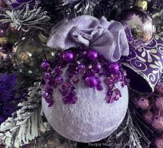 a purple ornament hanging from a christmas tree with ornaments around it and other decorations