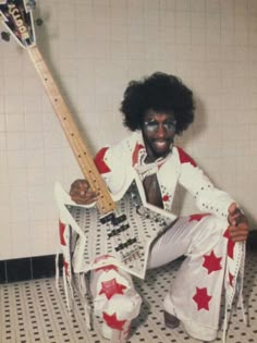 a man with an afro holding a guitar in his hand and posing for the camera