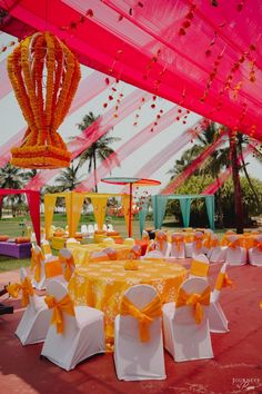 an orange and white wedding set up in a tent with yellow sashes on the tables