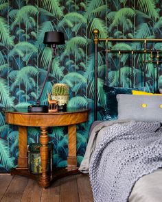 a bedroom with a bed, table and wallpaper that has green palm leaves on it