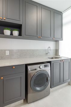 a washer and dryer in a kitchen with gray cabinets, white counter tops