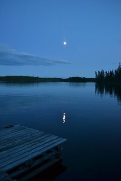 a full moon is seen in the sky over water with a wooden dock on it