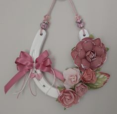 a white horseshoe decorated with flowers and pink ribbon hanging on a wall ornament