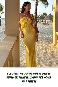 a woman in a yellow dress standing on the beach with her arms around her waist